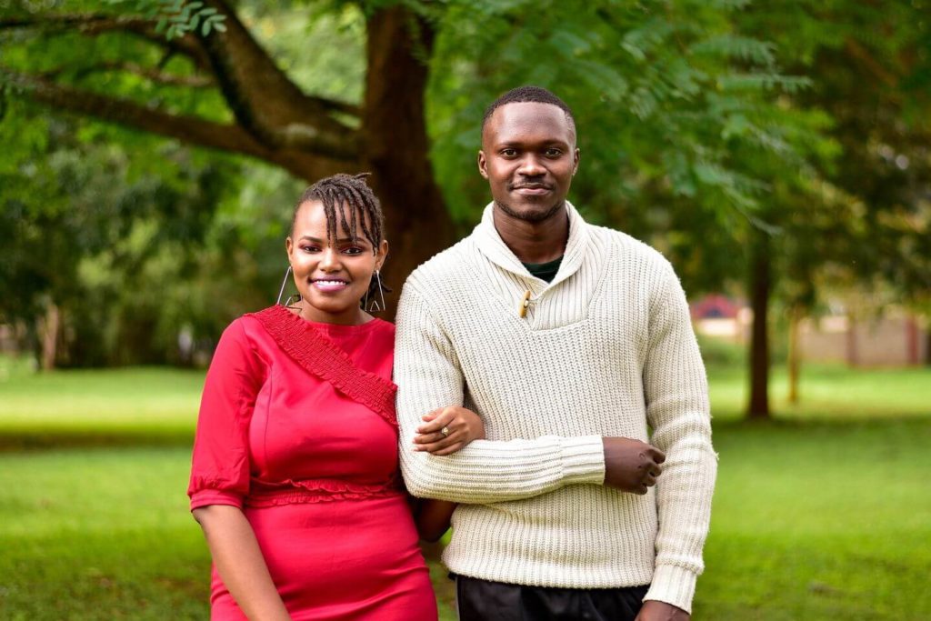A smiling couple standing outdoors with trees in the background, dressed in what to wear in Kenya.