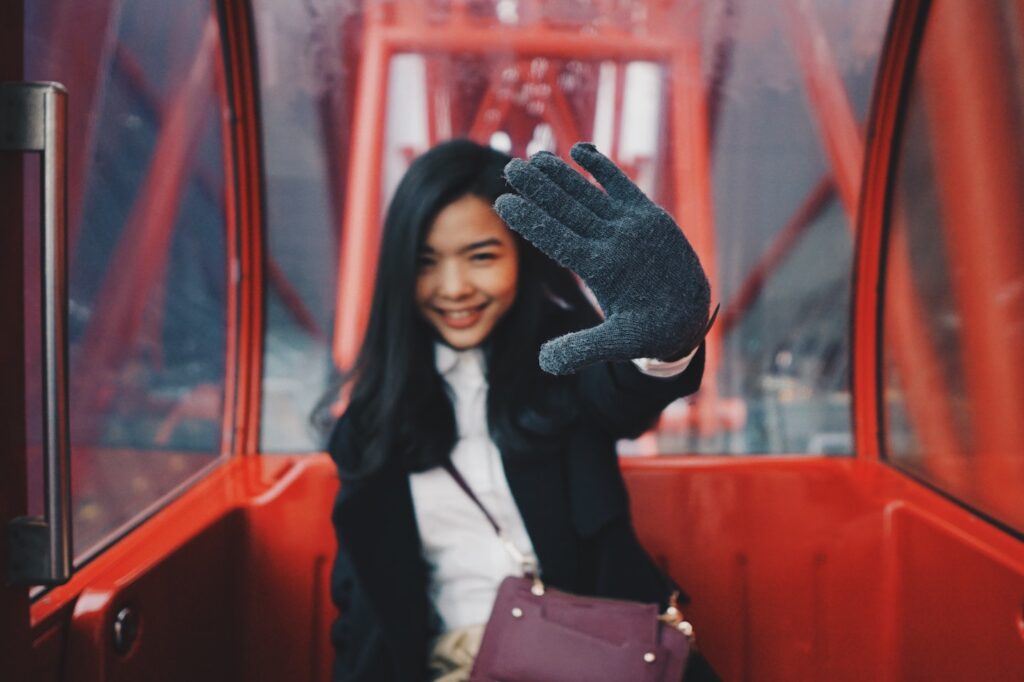 A woman in a cable car smiles and waves at the camera with a gloved hand, essential for her Japan packing list, with the interior of the car in red tones.